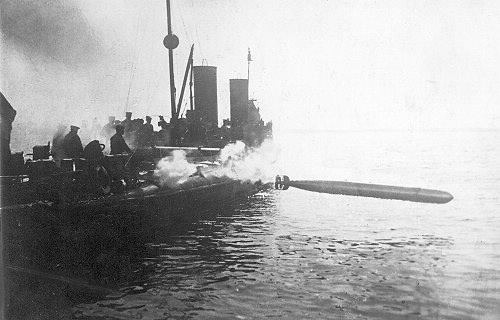 Moment odpalenia torpedy Whitehead model 5 kalibru 450 mm z dwururowej wyrzutni na jednym z austro-węgierskich 250-tonowych torpedowców typu "76 T", "82 F" lub "98 M." Podstawowe uzbrojenie torpedowe na jednostkach c.k. floty składało się z kilku podwójnych wyrzutni torpedowych kalibru 450 mm produkcji firmy "Whitehead? w Fiume (dzisiejsza chorwacka "Torpeda?, Rijeka.). Od roku 1907 wyrzutnie torpedowe na wszystkich c.k. torpedowcach, kontrtorpedowcach i krążownikach ogrzewane mogły być parą, co zapobiegało zamarzaniu głowic torpedowych. Same torpedy należały do typu Whitehead kal. 450 mm L/5 o długości 5,25 m i masie 744 kg, z czego 130 kg przypadało na ładunek wybuchowy znajdujący się w jej głowicy. Napęd stanowił silnik tłokowy zasilany sprężonym powietrzem o ciśnieniu 150 atm. (15,2 Mpa) połączony wałem z dwiema śrubami przeciwbieżnymi. Maksymalna prędkość torpedy wynosiła 40 w, a maksymalny zasięg to 1500 m. Po podgrzaniu powietrza w zbiorniku za pomocą przyrządów grzejnych Armstronga zasięg tej groźnej broni wzrastał o 15%.  Źródło: mateinfo.hu